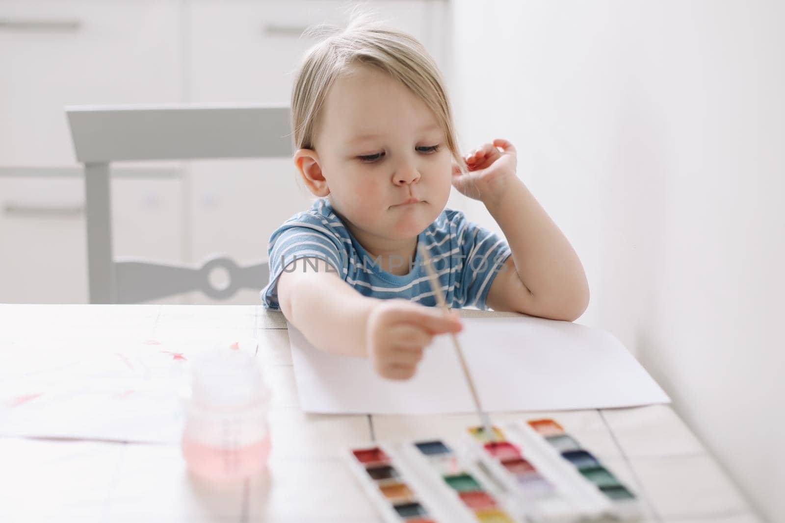 Child painting and drawing with watercolor paint at white table. Development of creative potential in children