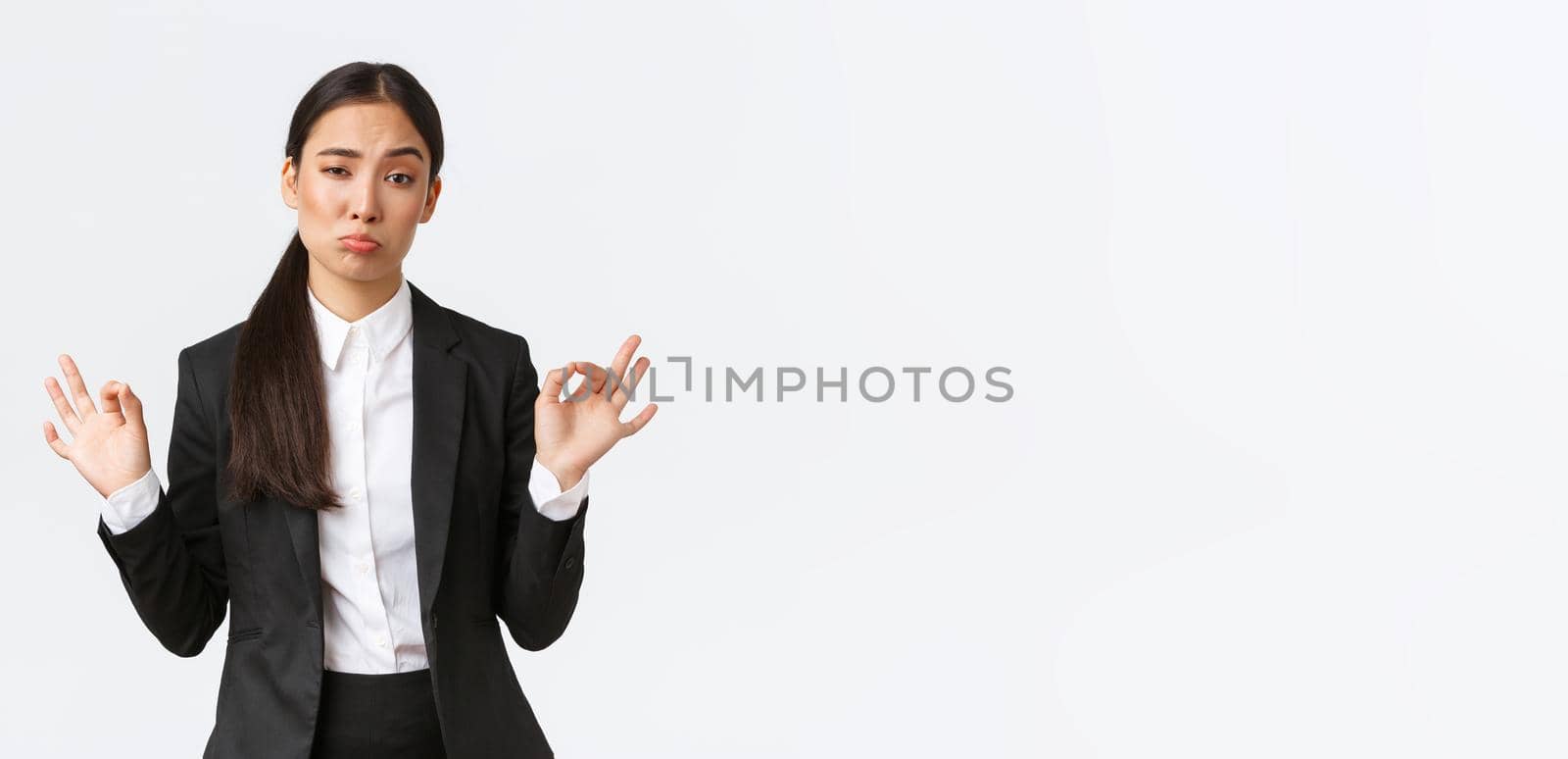 Pleased sassy asian businesswoman in black suit show not bad gesture, nod in approval and make okay gesture, very good work, praising coworker, standing satisfied over white background by Benzoix