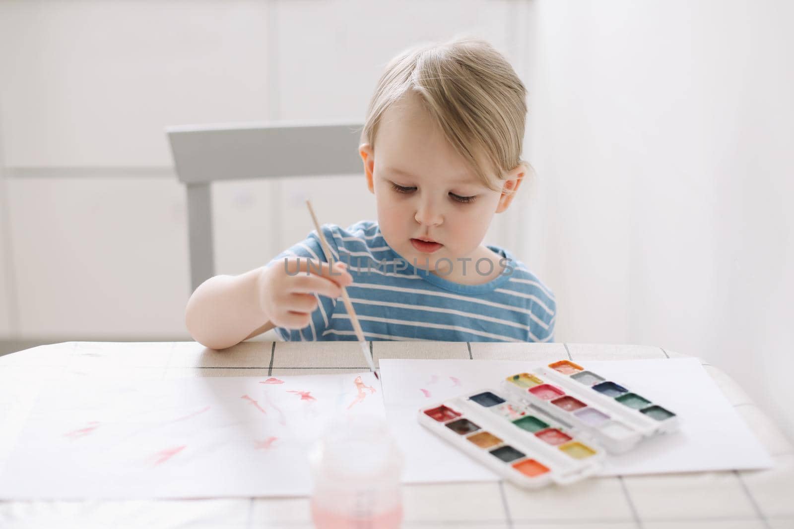 Child painting and drawing with watercolor paint at white table. Development of creative potential in children