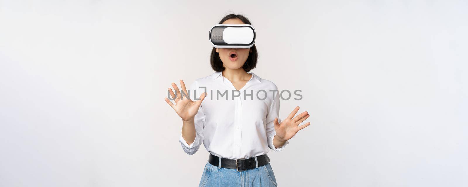 Amazed young woman in virtual reality, using vr glasses headset, standing over white background. Technology concept