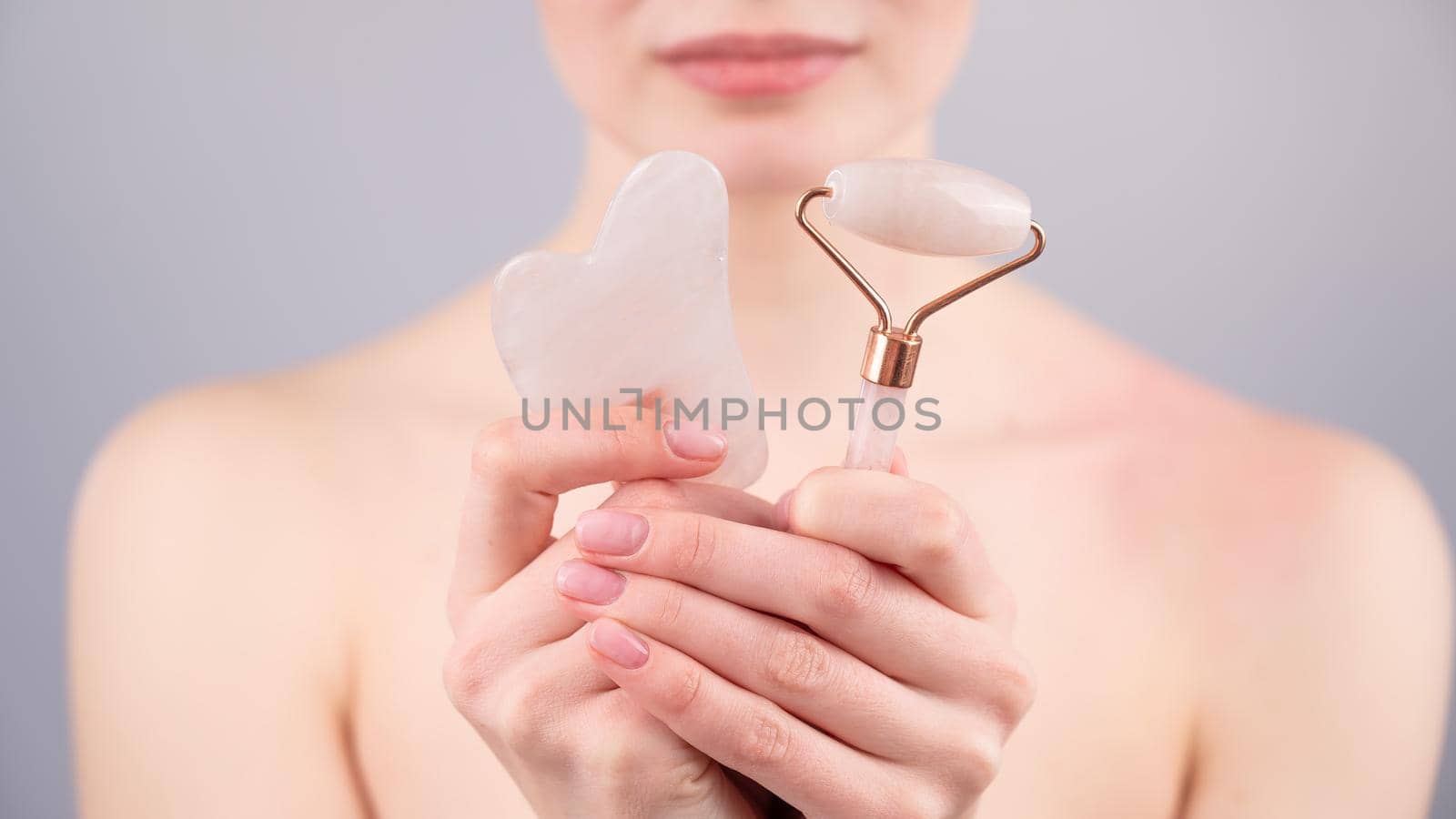 Caucasian woman holding pink roller massager and gouache scraper on white background