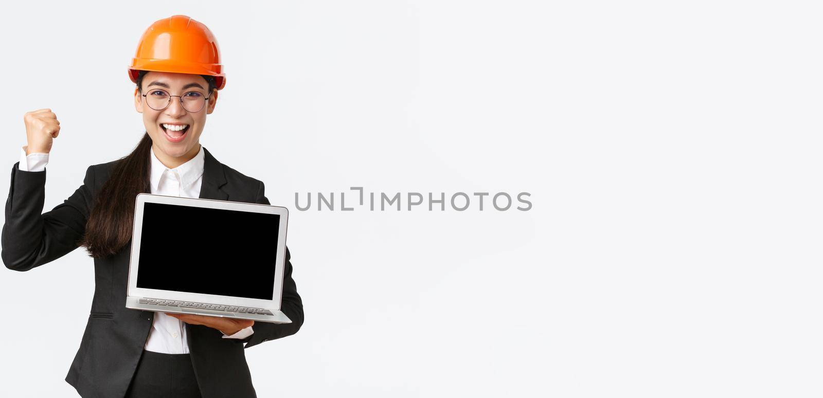 Successful winning businesswoman, construction manager or engineer at factory showing profit chart, diagram at laptop screen, fist pump in rejoice, standing pleased over white background by Benzoix