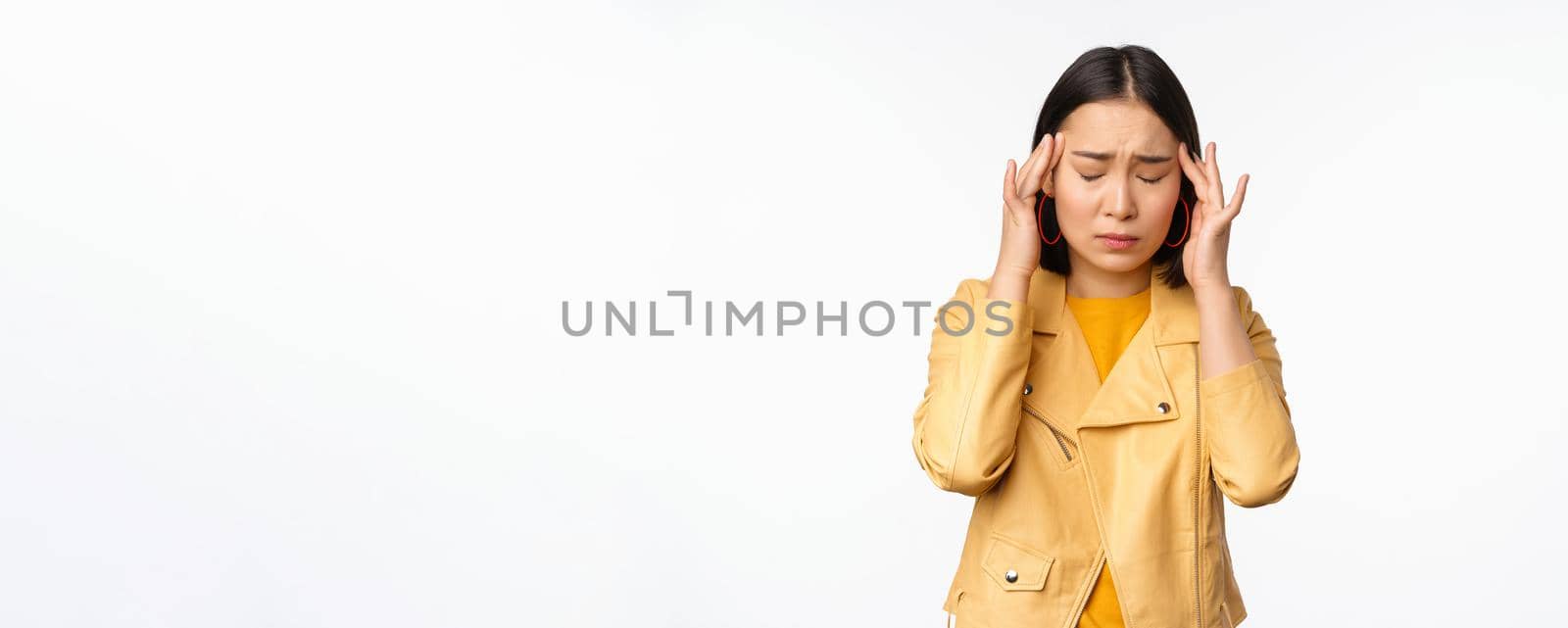 Image of asian woman massaging head temples with concerned face, suffering headache, migraine, standing over white background.