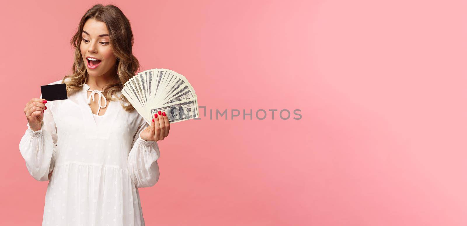 Portrait of rich good-looking blond girl in white dress, holding dollars money and credit card, winning lottery, think how invest, standing happy pink background by Benzoix