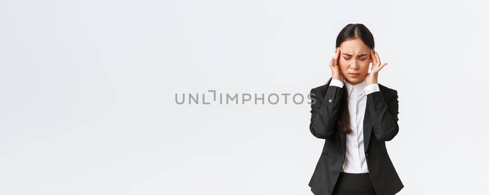 Businesswoman trying to focus, suffering migraine before important business meeting. Asian female entrepreneur touching temples and grimacing from pain, having headache, white background.