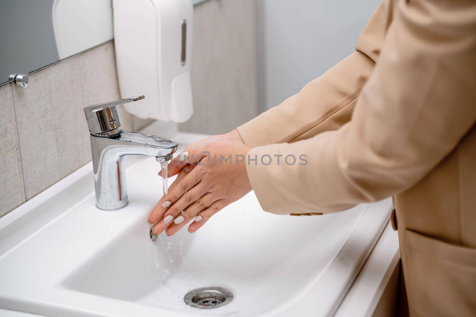 A woman washes her hands under running tap water in a public toilet. by Matiunina