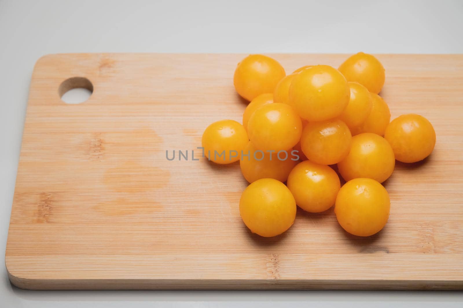 A heap of yellow cherry tomatoes on a wooden cutting board in the kitchen on a white table.