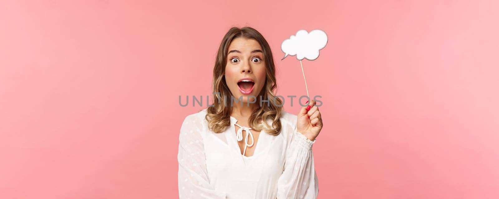 Spring, happiness and celebration concept. Close-up portrait of surprised, excited blond girl looking amazed, holding cloud comment stick near head and gasping astonished, have idea, pink background by Benzoix