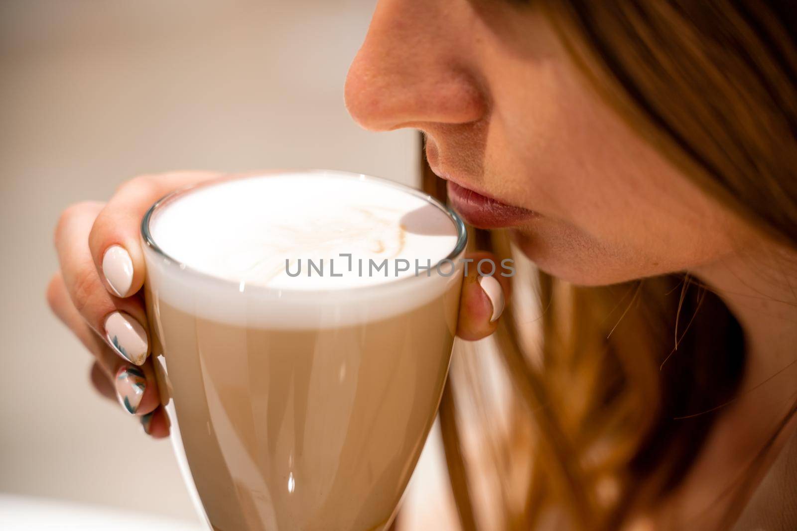 Close-up of beautiful female hands holding a large white cup of cappuccino. A woman is sitting in a cafe