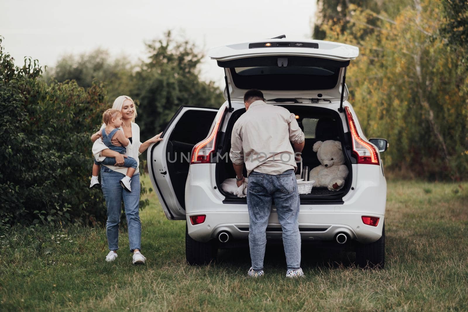 Two Parents with Their Little Kid Preparing to Picnic Time Outdoors, Young Family Enjoying Road Trip on the SUV Car by Romvy