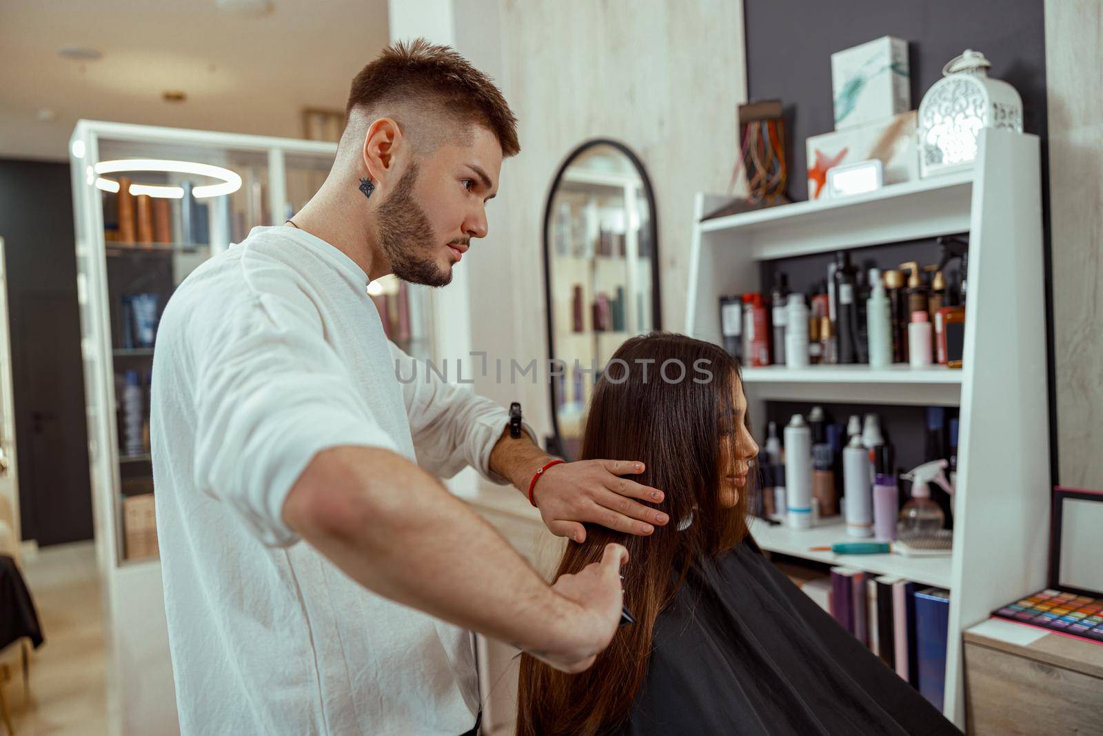 Professional male hairdresser brushing long brown hair of female client, making hairstyle at beauty salon by Yaroslav_astakhov