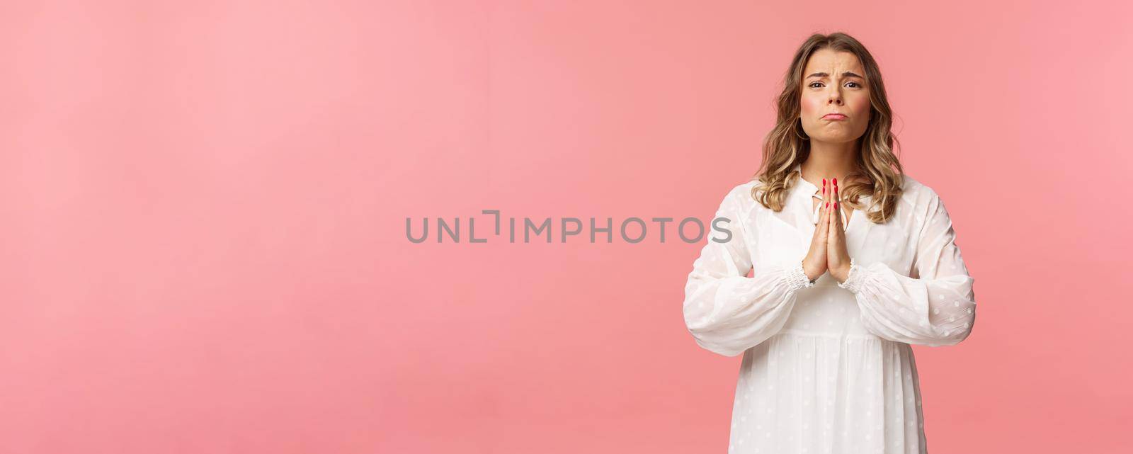 Portrait of hopeful clingy girlfriend, blond girl begging for favour in white dress over pink background, sobbing make cute eyes, pleading or praying, say please, want something badly.