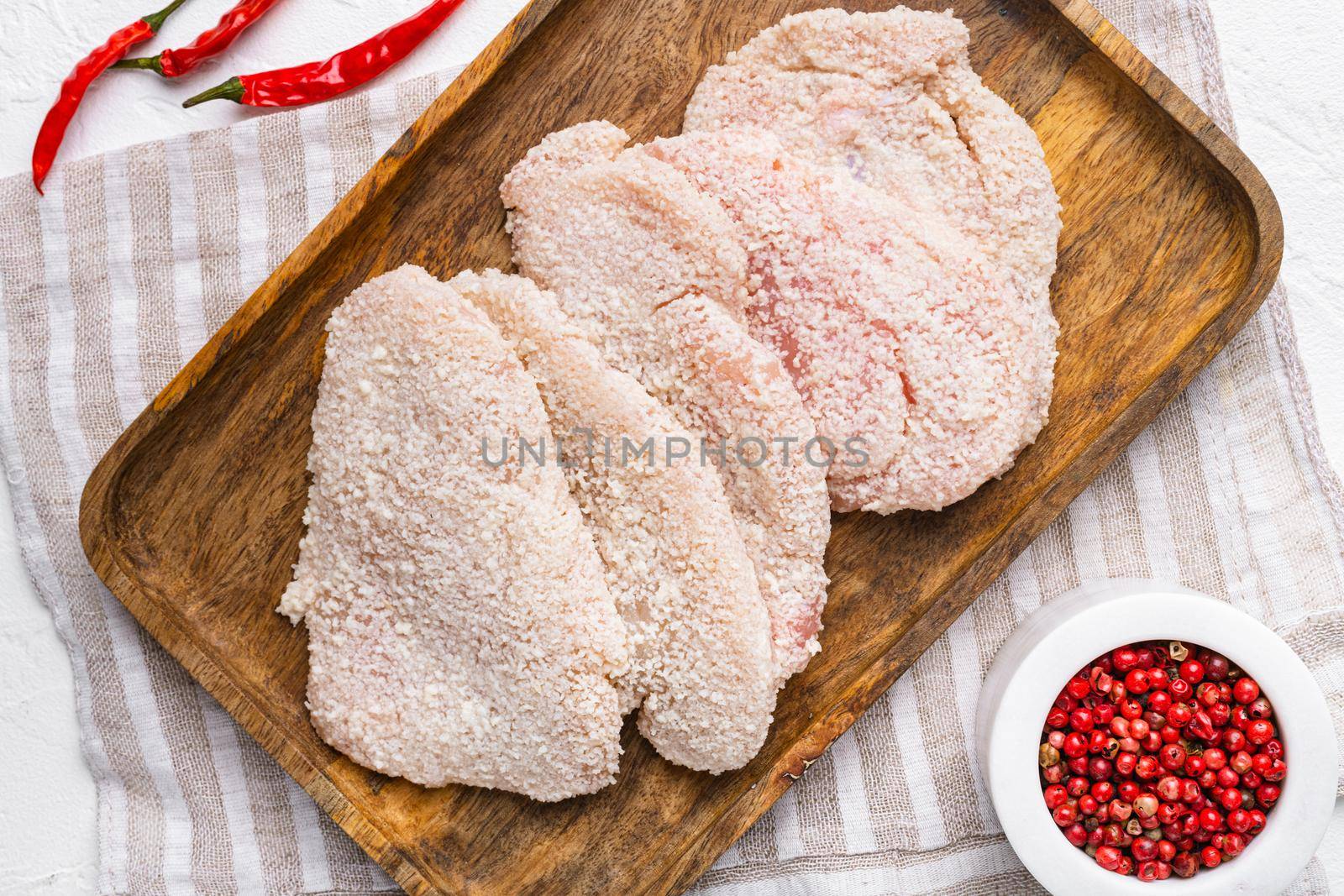 Raw chicken schnitzel in breadcrumbs, on white stone table background, top view flat lay