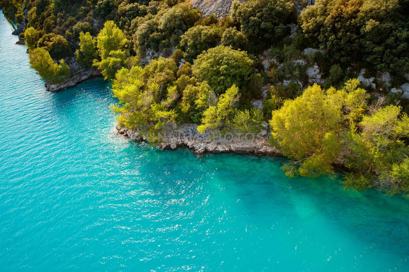 azure water of the lake and slopes of mountains on a background, coast line, green trees, sun light. High quality photo