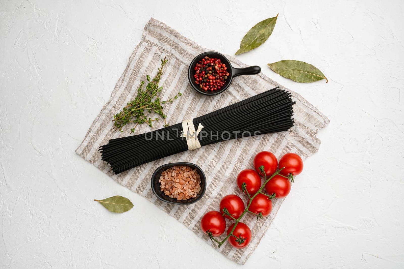 Black colored spaghetti raw dry set, on white stone table background, top view flat lay