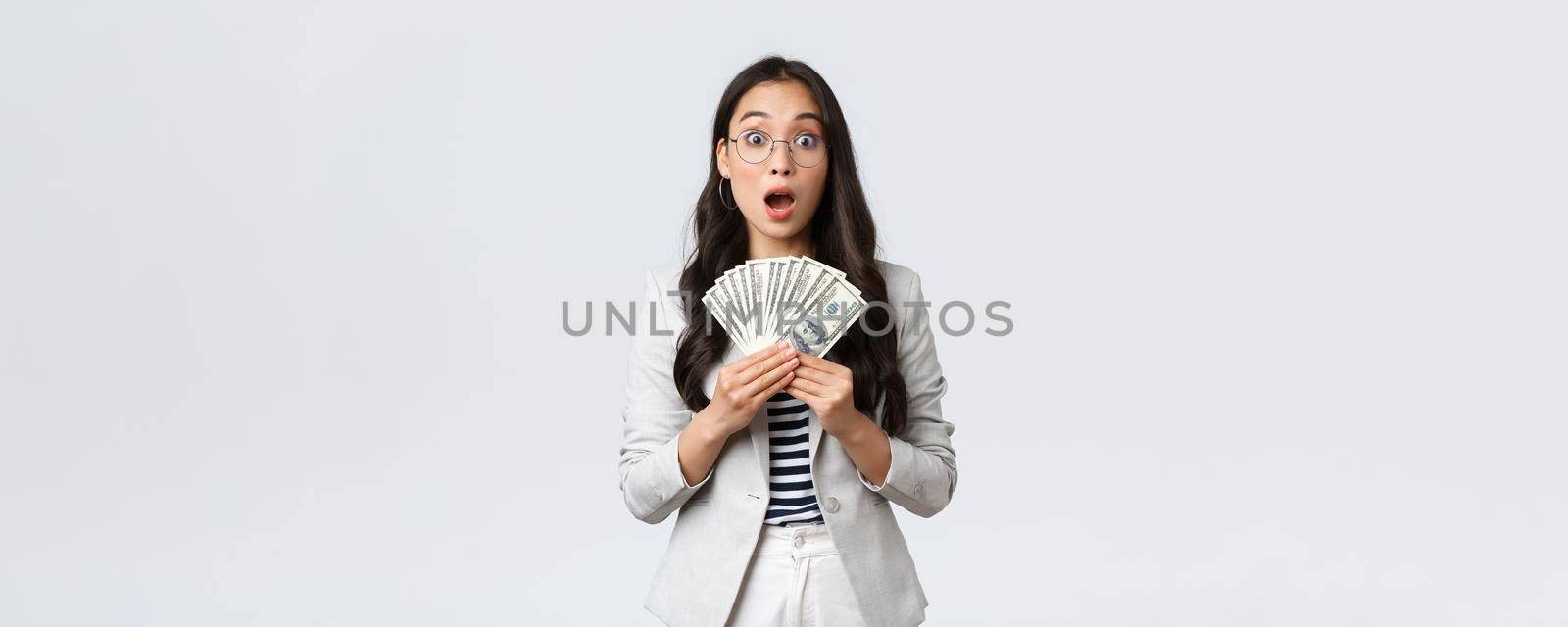 Business, finance and employment, entrepreneur and money concept. Amazed and speechless young asian businesswoman earn first paycheck for selling house, holdin cash and stare astonished.