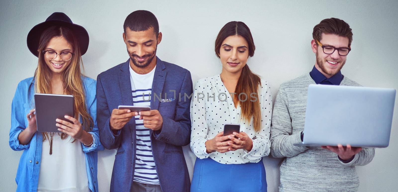 Catch up on social media while you wait. Studio shot of a group of young businesspeople using wireless technology while standing in line against a grey background. by YuriArcurs