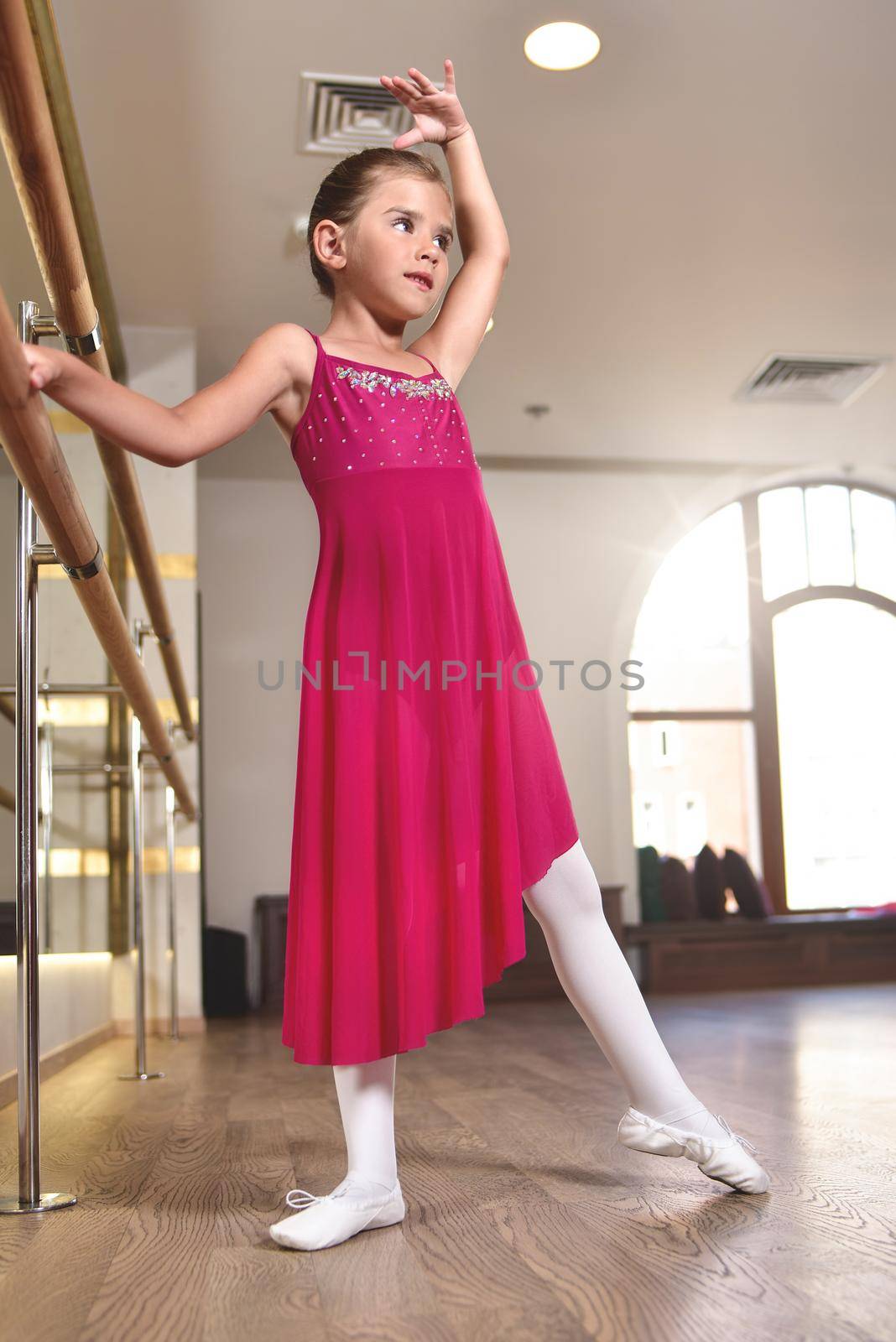 charming little girl dreams of becoming a ballerina. The girl in the pink dress is dancing, holding on to the bar.Baby girl is studying ballet. by Nickstock