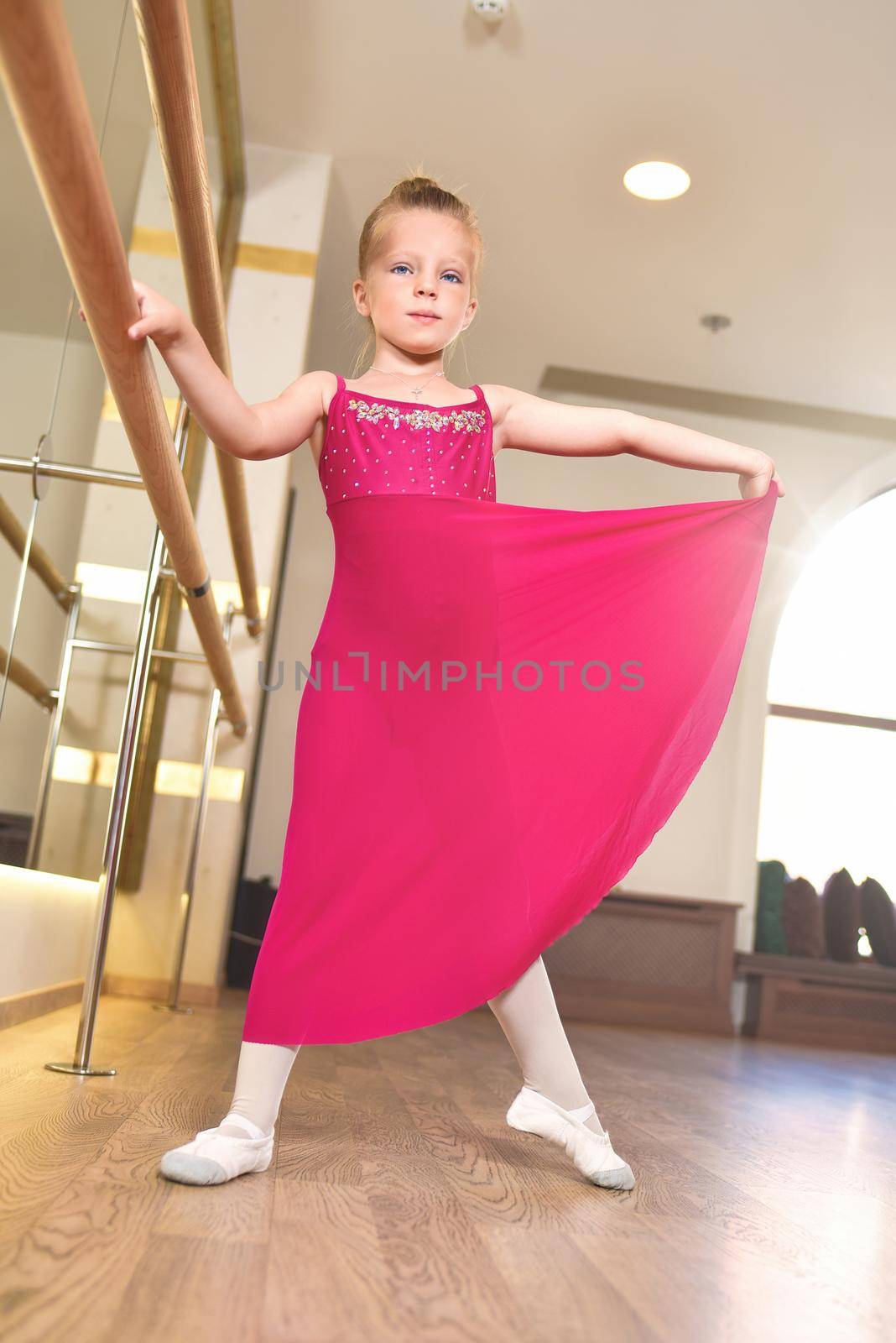 the charming little girl dreams of becoming a ballerina. The girl in the pink dress is dancing, holding on to the bar.Baby girl is studying ballet.