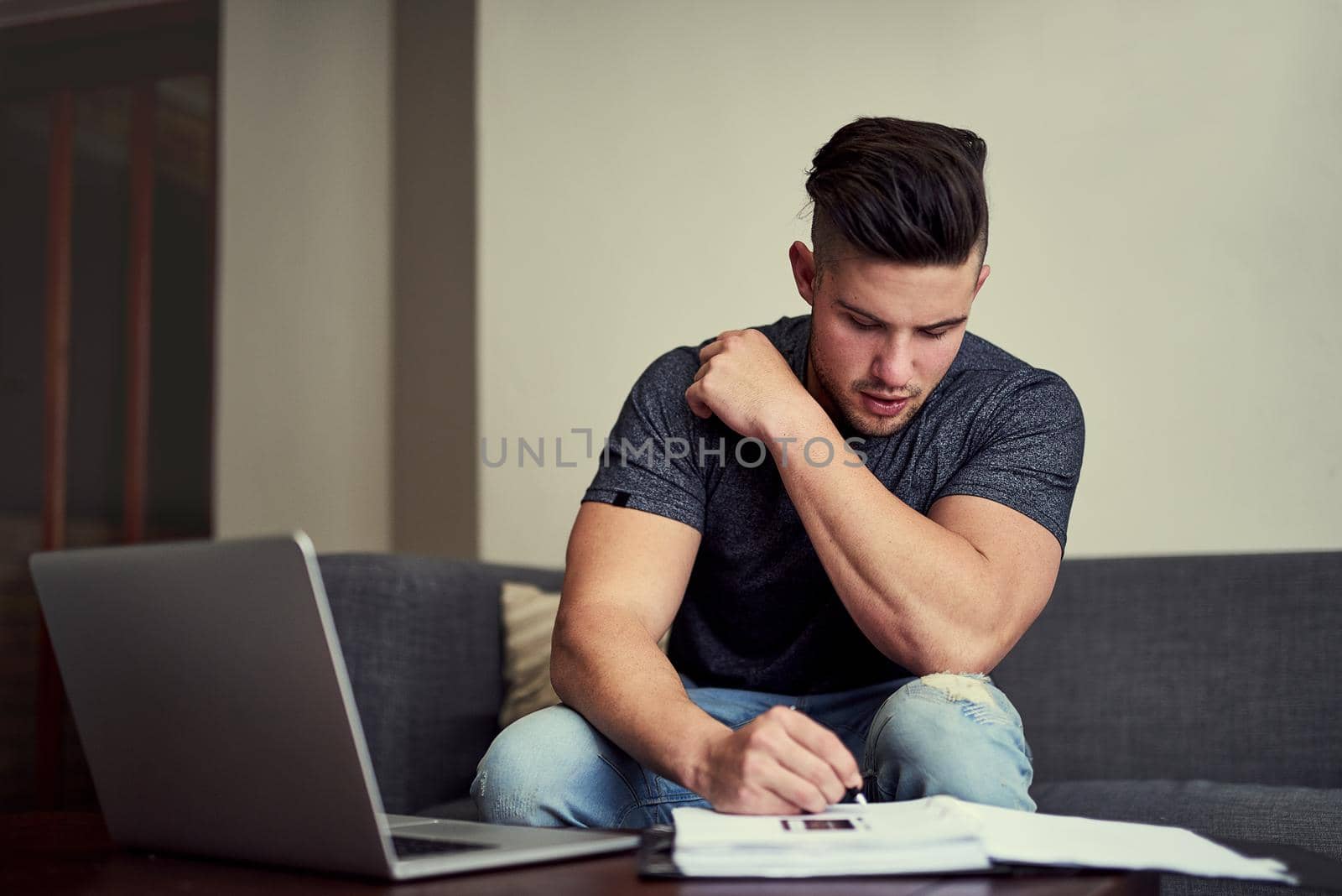 Working hard to distinguish himself from the rest. Shot of a driven young man using his laptop to work from home. by YuriArcurs