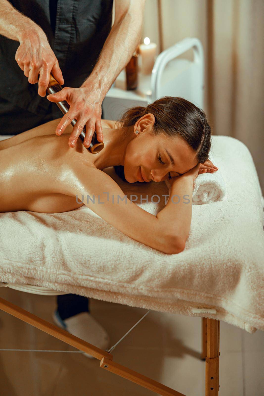 Happy female client getting back massage with hollow bamboo canes at spa salon. Therapy