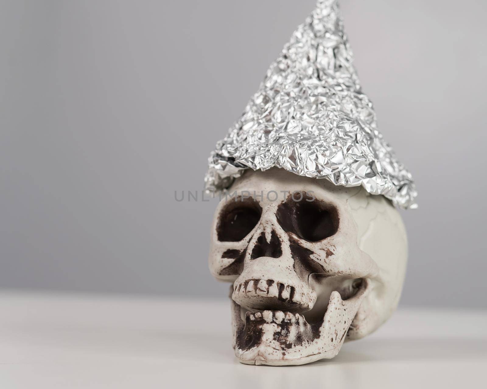 Plastic skull in a tinfoil cap on a white background. by mrwed54