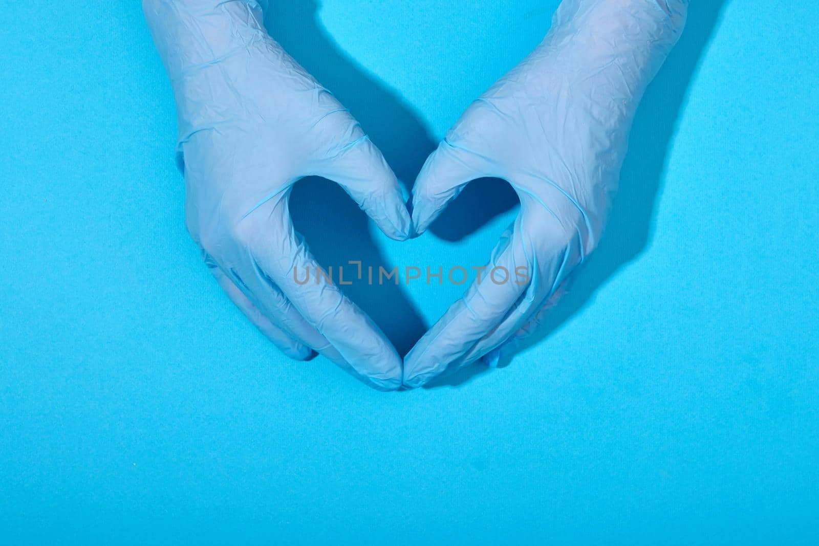Doctors hands in medical gloves in shape heart blue background by Demkat