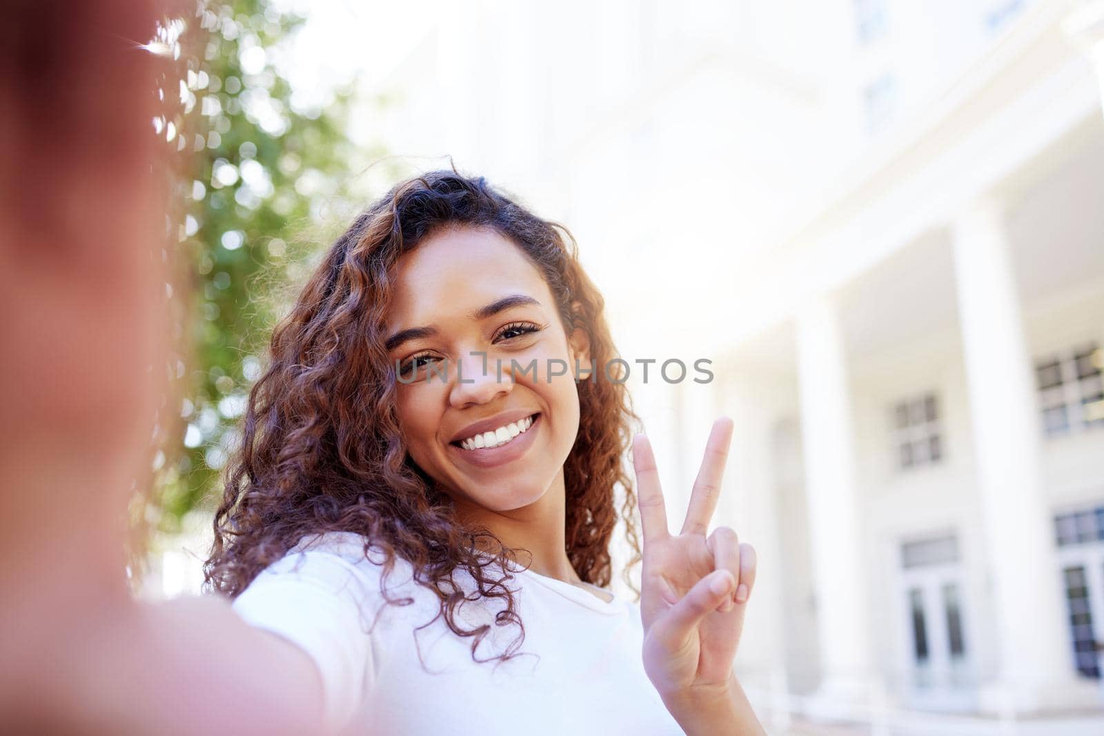 Shot of a female showing a peace gesture while taking a selfie outside.