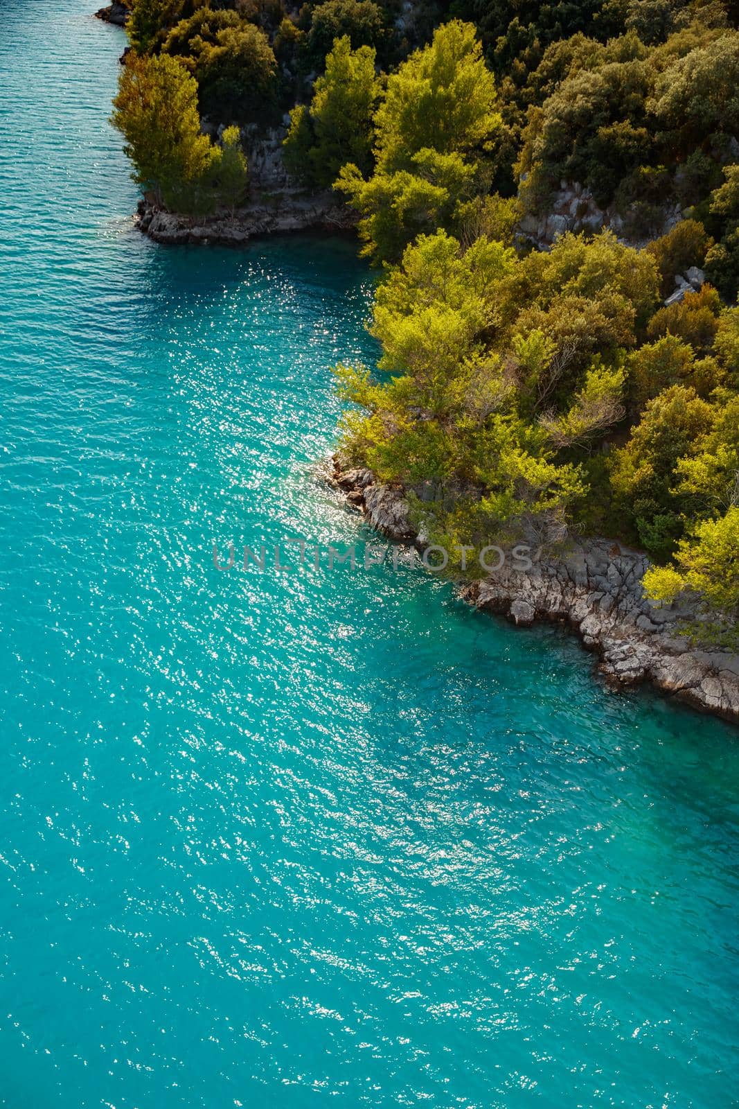 azure water of the lake and slopes of mountains on a background, coast line, green trees, sun light. High quality photo