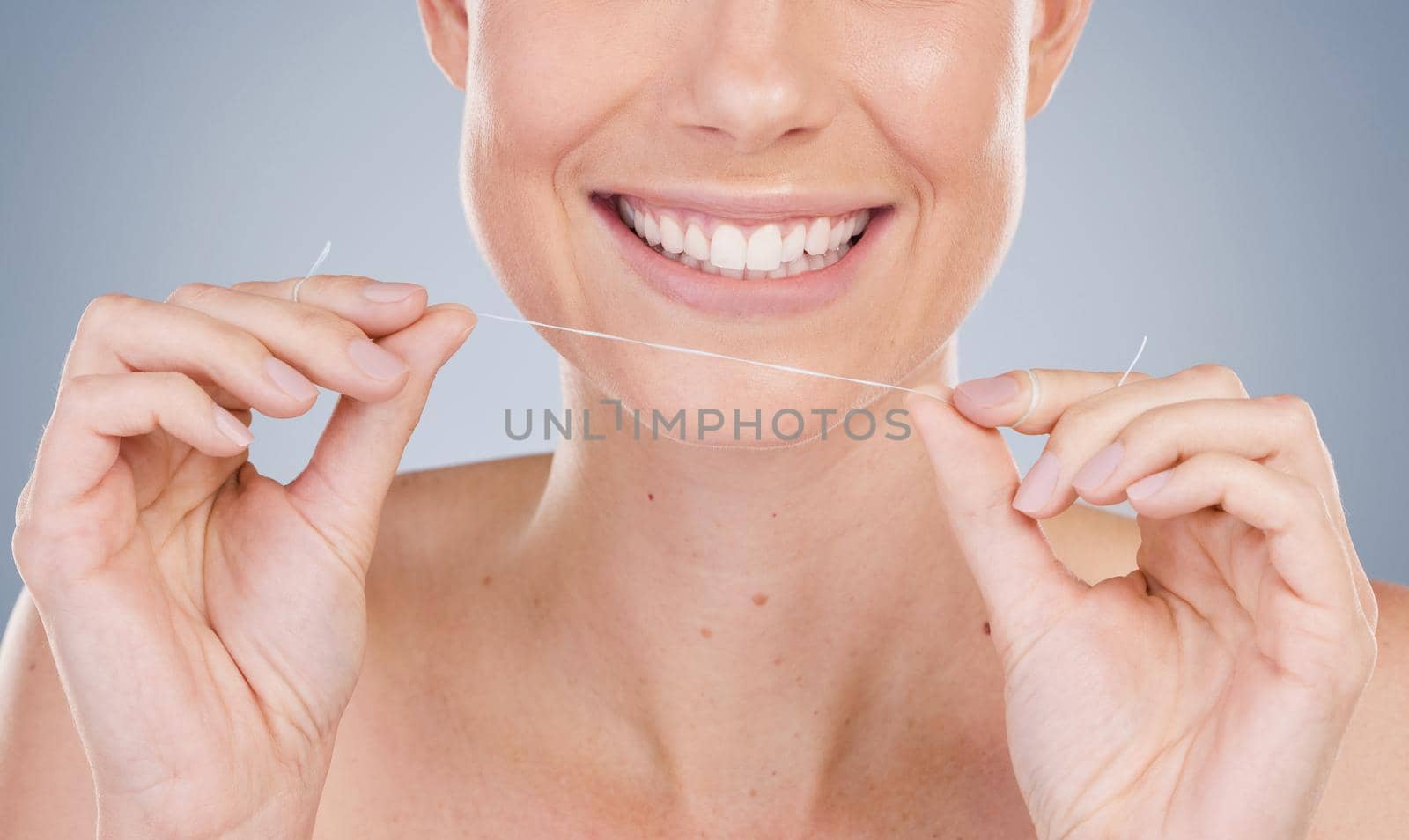 Studio shot of an unrecognizable young woman using dental floss against a grey background.
