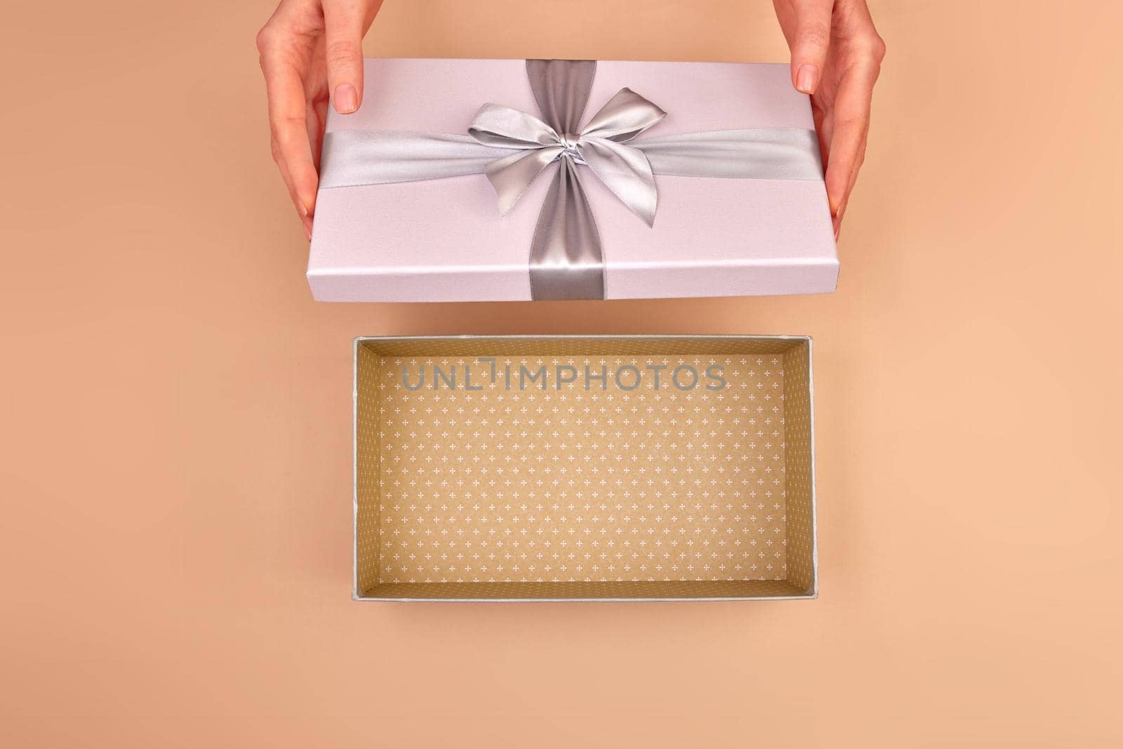 Female hands open a silver gray light box with a bow and you can see empty package beige delicate background top view