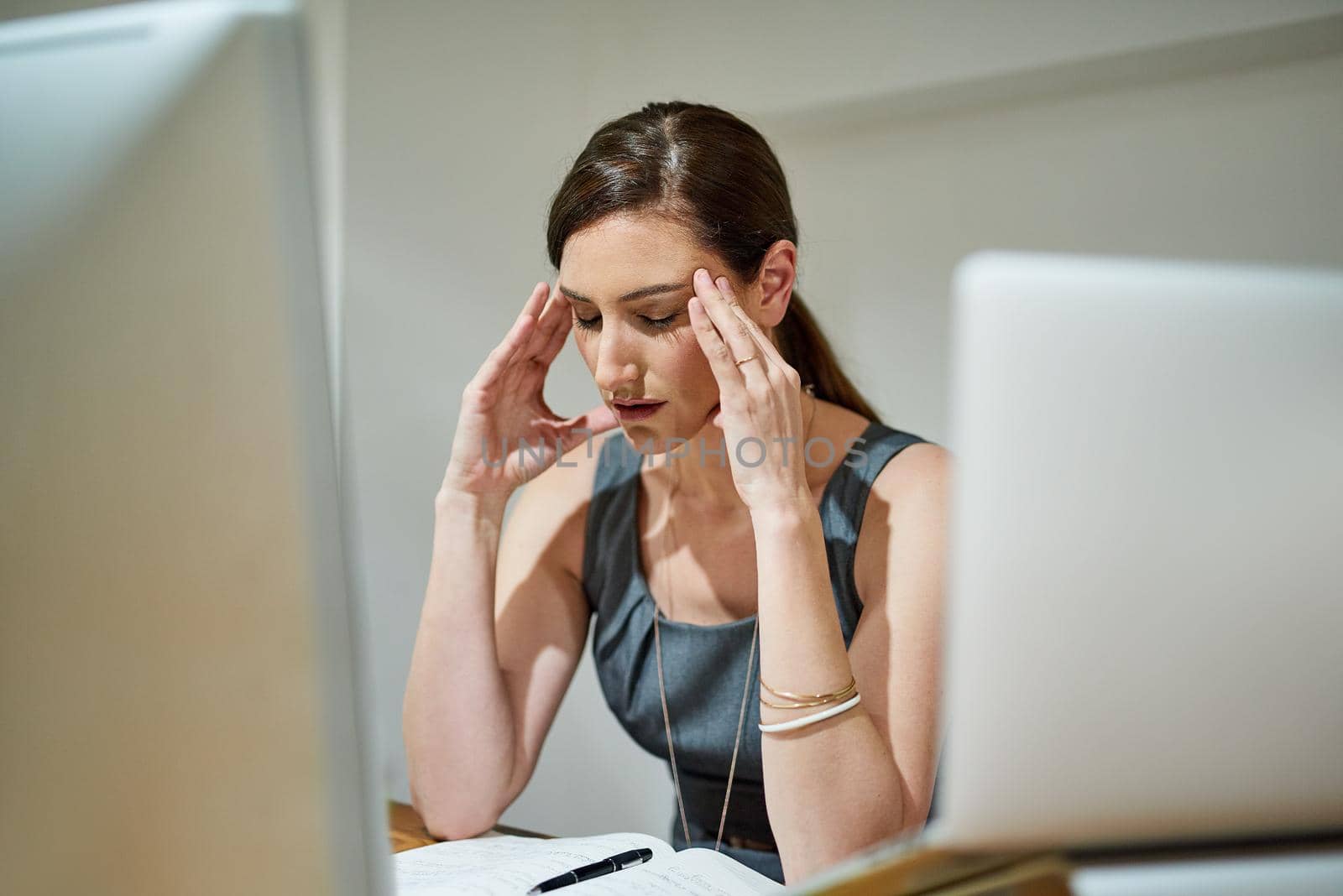 When work becomes too hard to handle. Shot of a businesswoman suffering from a headache at her office desk. by YuriArcurs