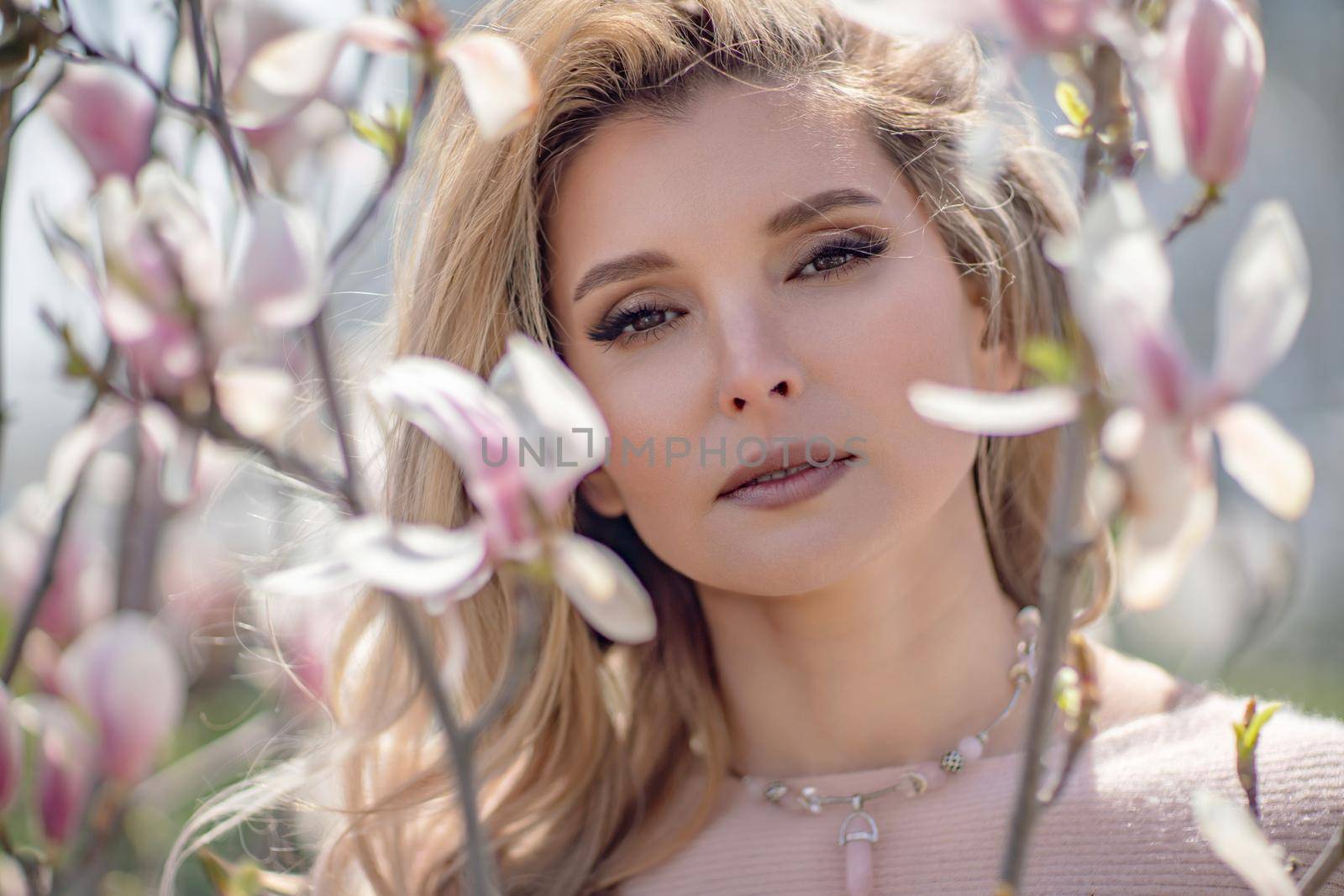 Portrait of a beautiful happy middle aged woman enjoying the smell in a blooming spring garden. Beautiful magnolia bushes, large flowers. by Matiunina