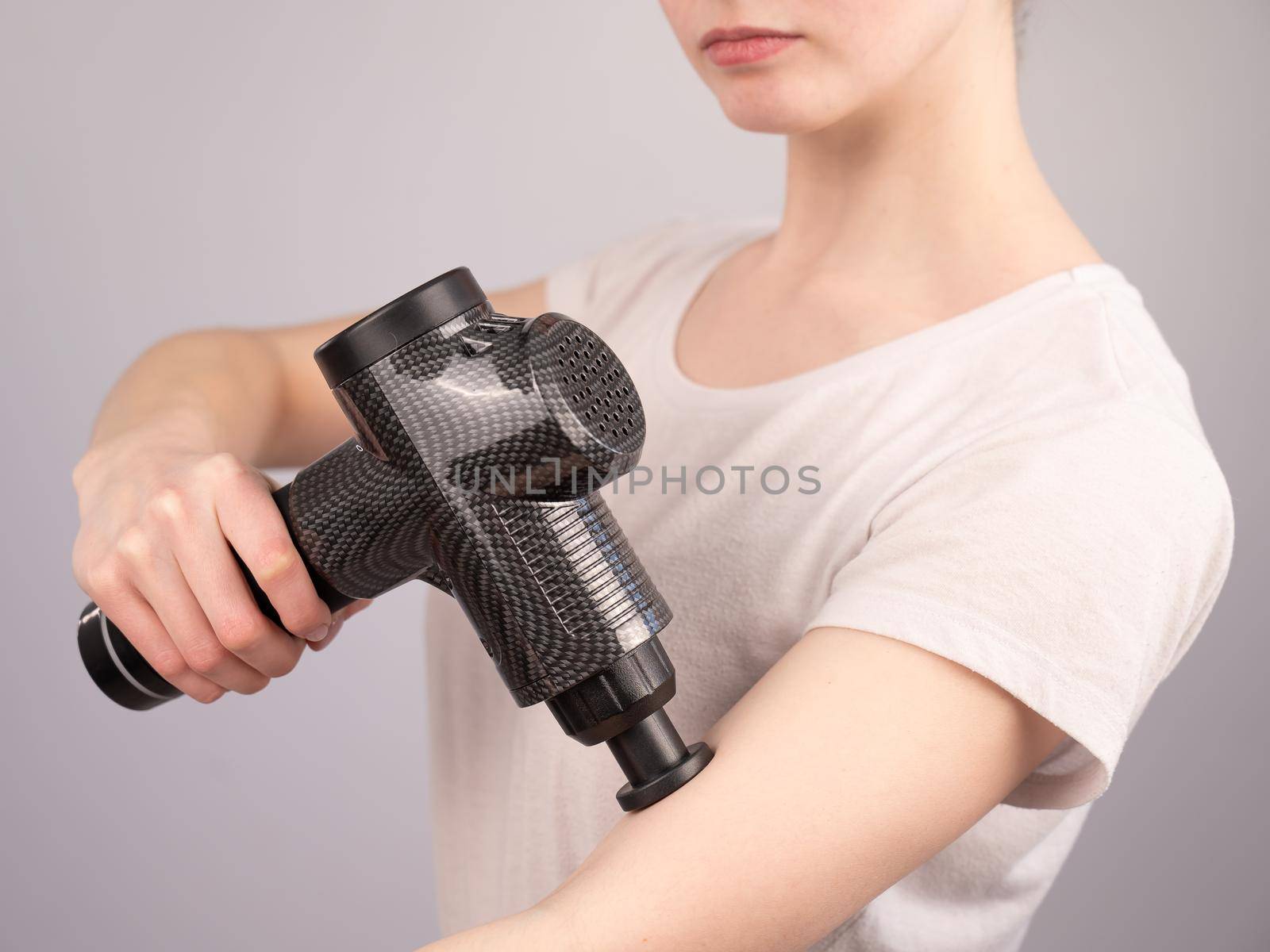 Caucasian woman uses a massager gun for pain in the muscles of the arm