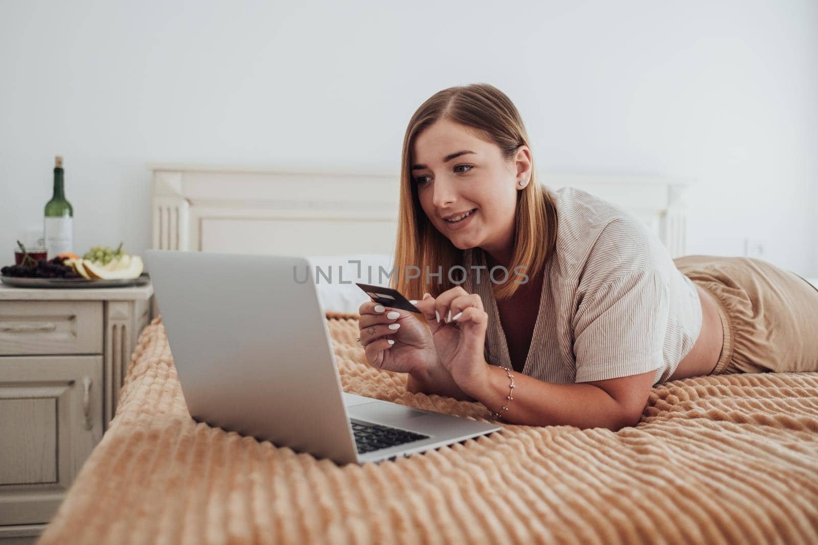 Caucasian Young Woman Making Online Shopping Through Laptop While Laying on Bed of Hotel Room