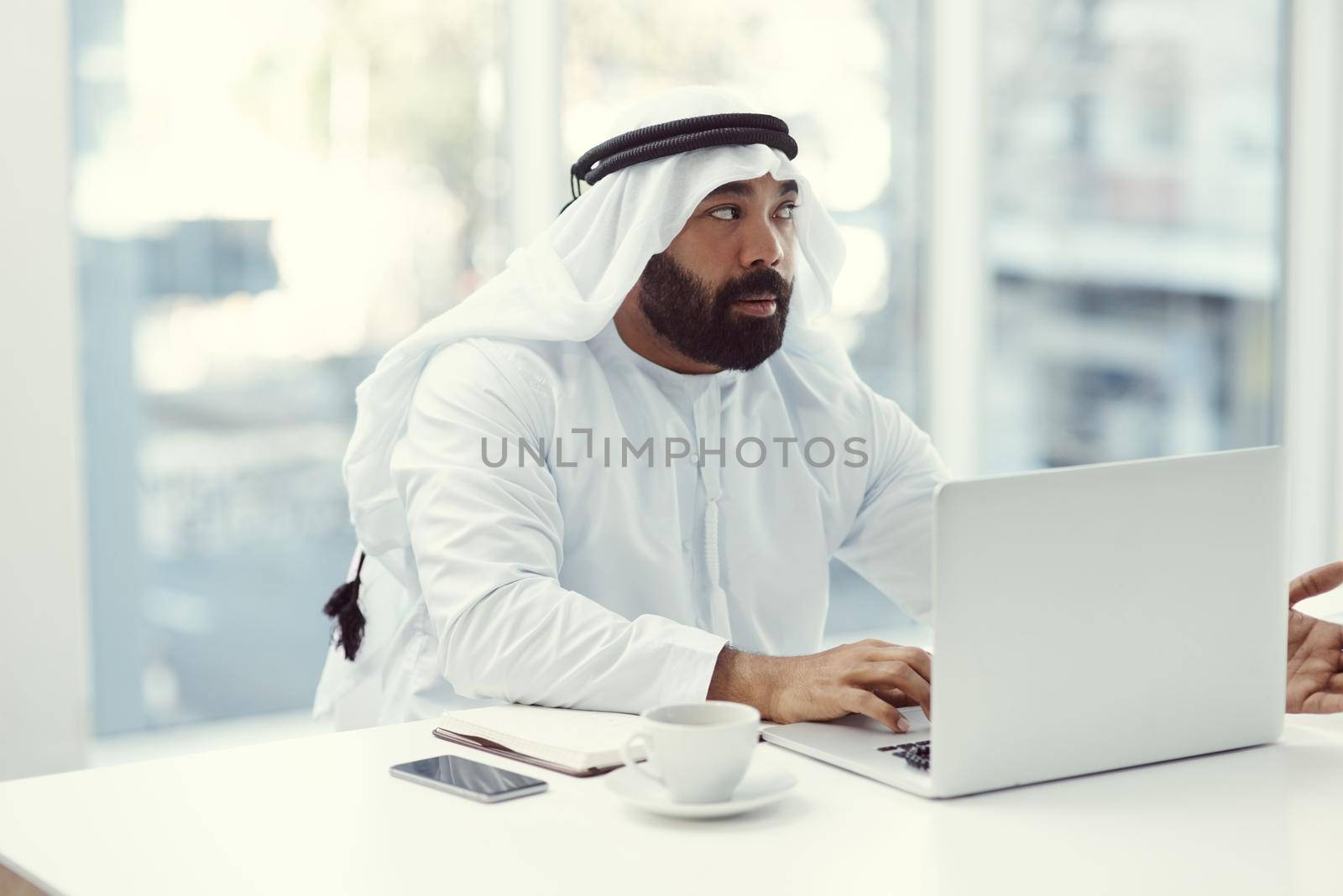 Hes got an idea. Cropped shot of a young businessman dressed in Islamic traditional clothing working on his laptop while sitting in the office. by YuriArcurs