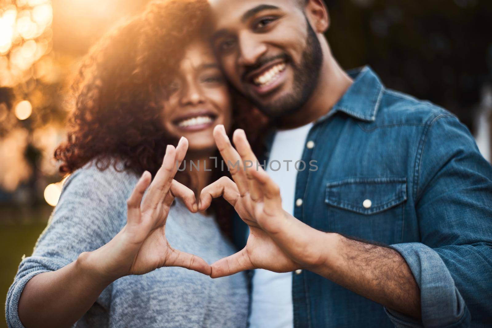 The heart knows what it wants. Portrait of a a young couple making a heart shape with their fingers outdoors. by YuriArcurs