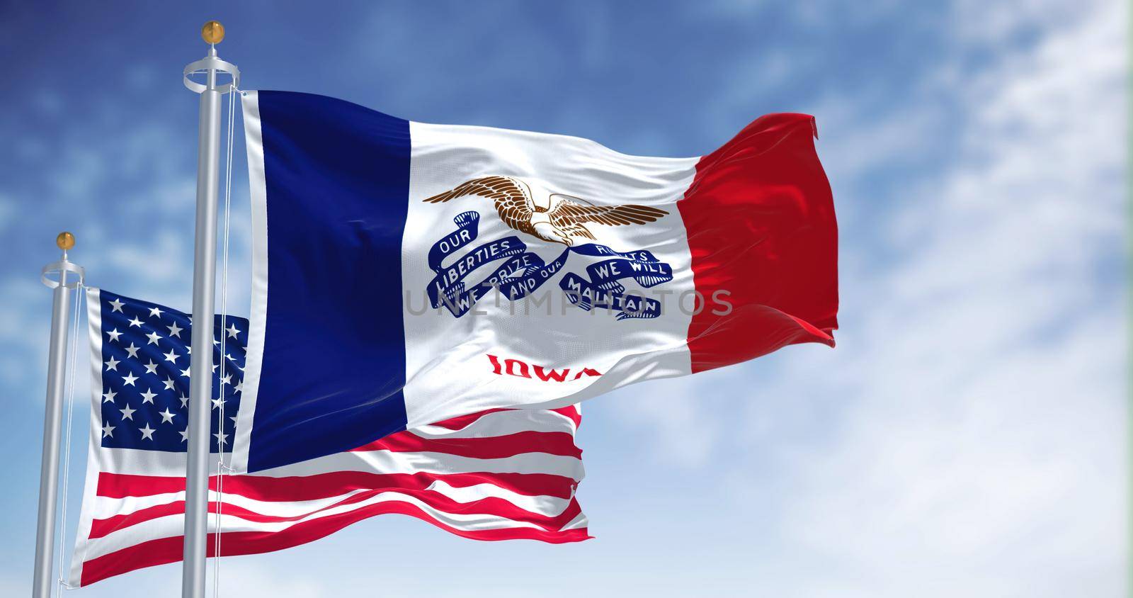 The Iowa state flag waving along with the national flag of the United States of America. In the background there is a clear sky. Iowa is a state in the Midwestern region of the United States