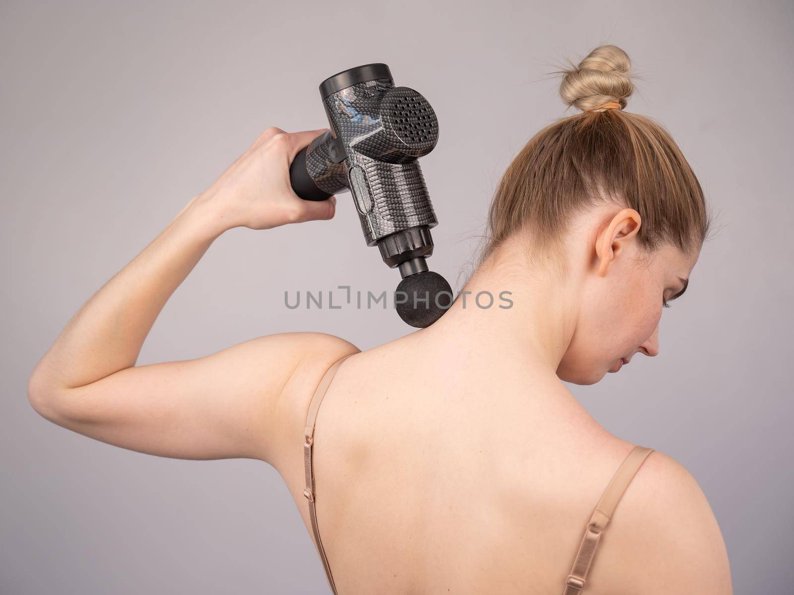 Caucasian woman giving herself a back massage with a gun