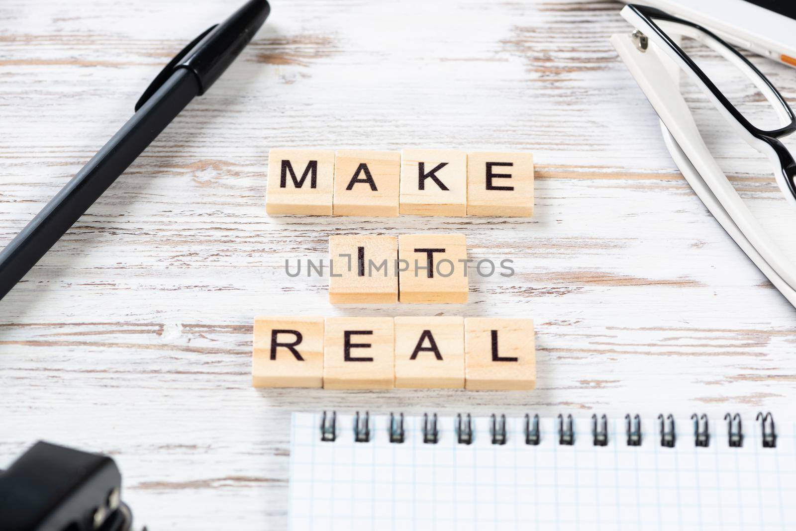 Make it real quote with letters on wooden cubes. Still life of office workspace. Flat lay vintage wooden desk with pen, glasses and spiral notebook. Business motivation and inspiration composition