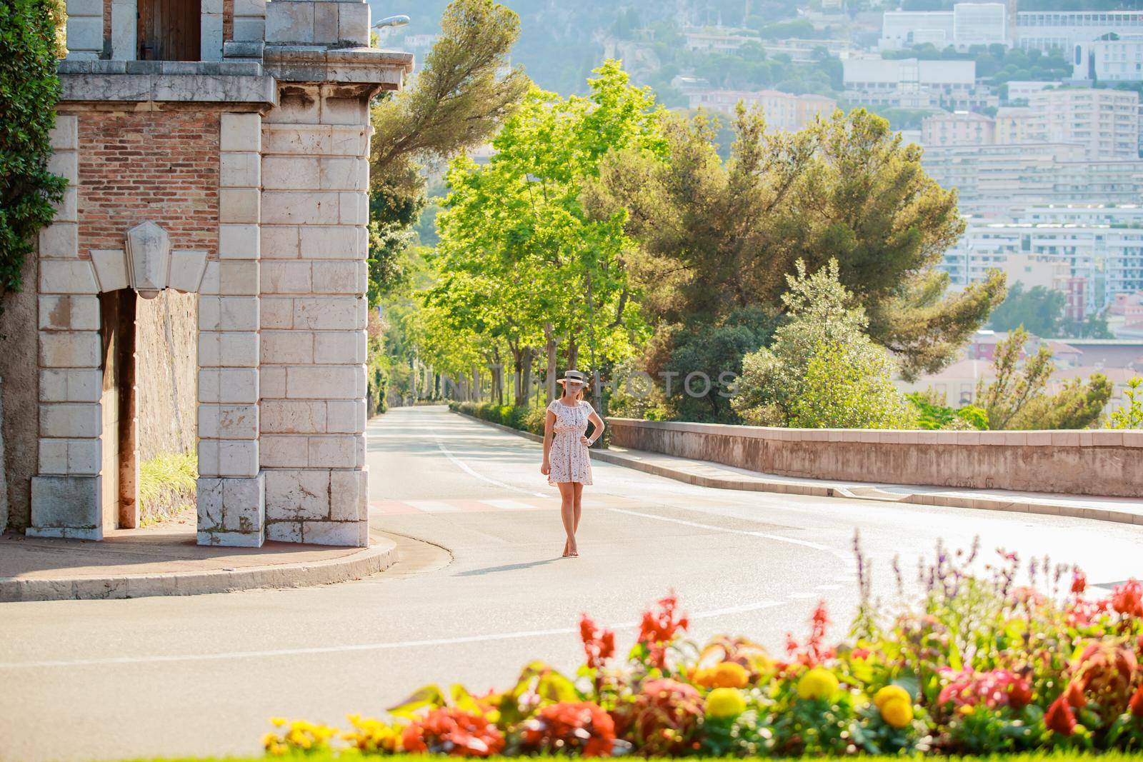 a bright beautiful girl in a light dress and hat walks along the streets of Monaco in sunny weather in the summer, luxury apartments of Monte Carlo on background by vladimirdrozdin