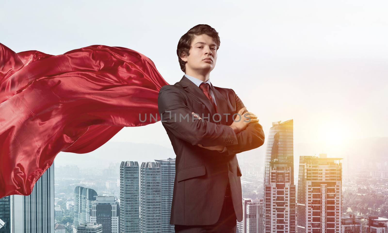 Young confident businessman wearing red cape against modern city background