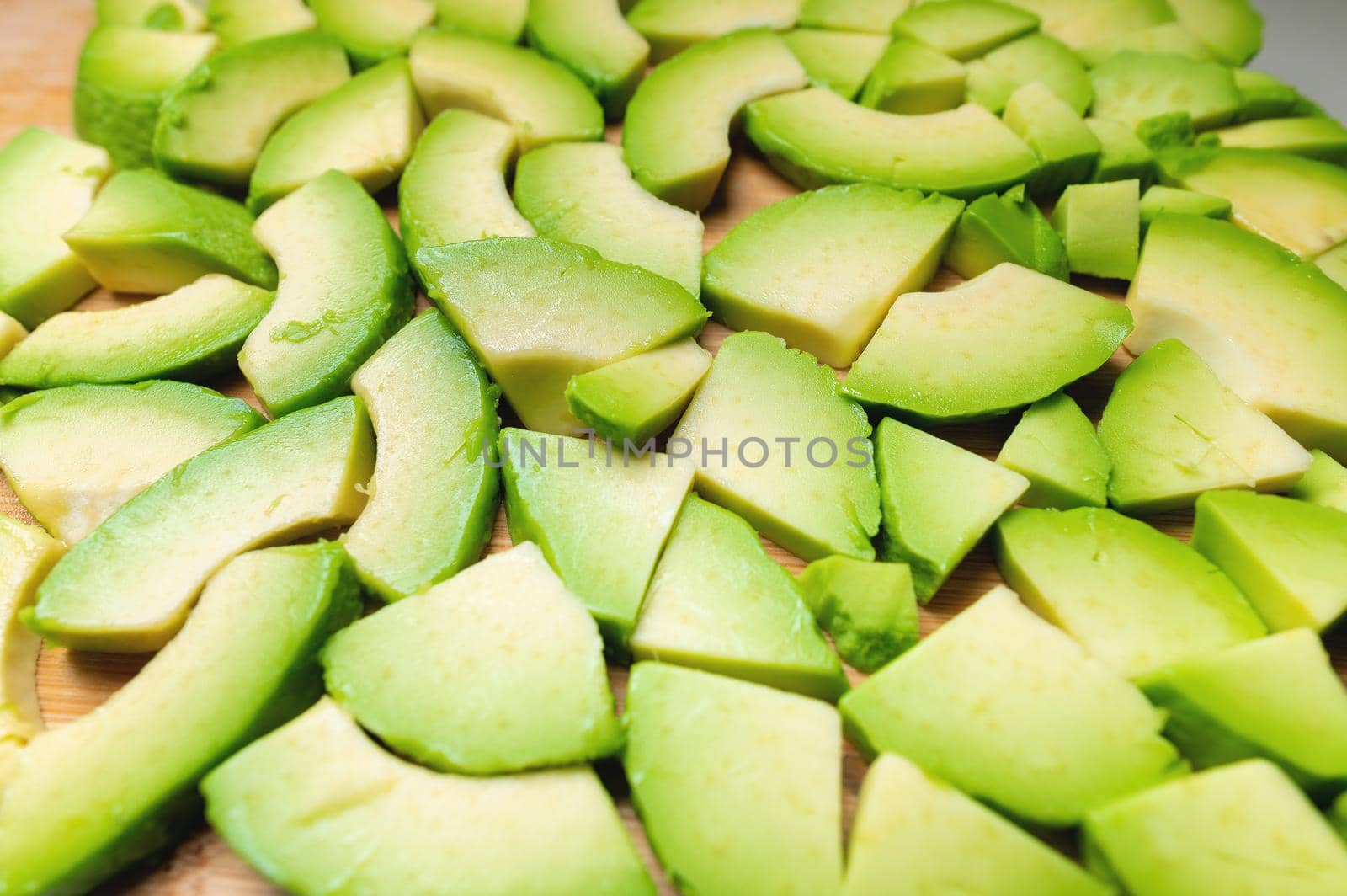 Fresh and tasty avocado cut into pieces laid out on a wooden cutting board. Vegetarian background fresh vegetables by yanik88