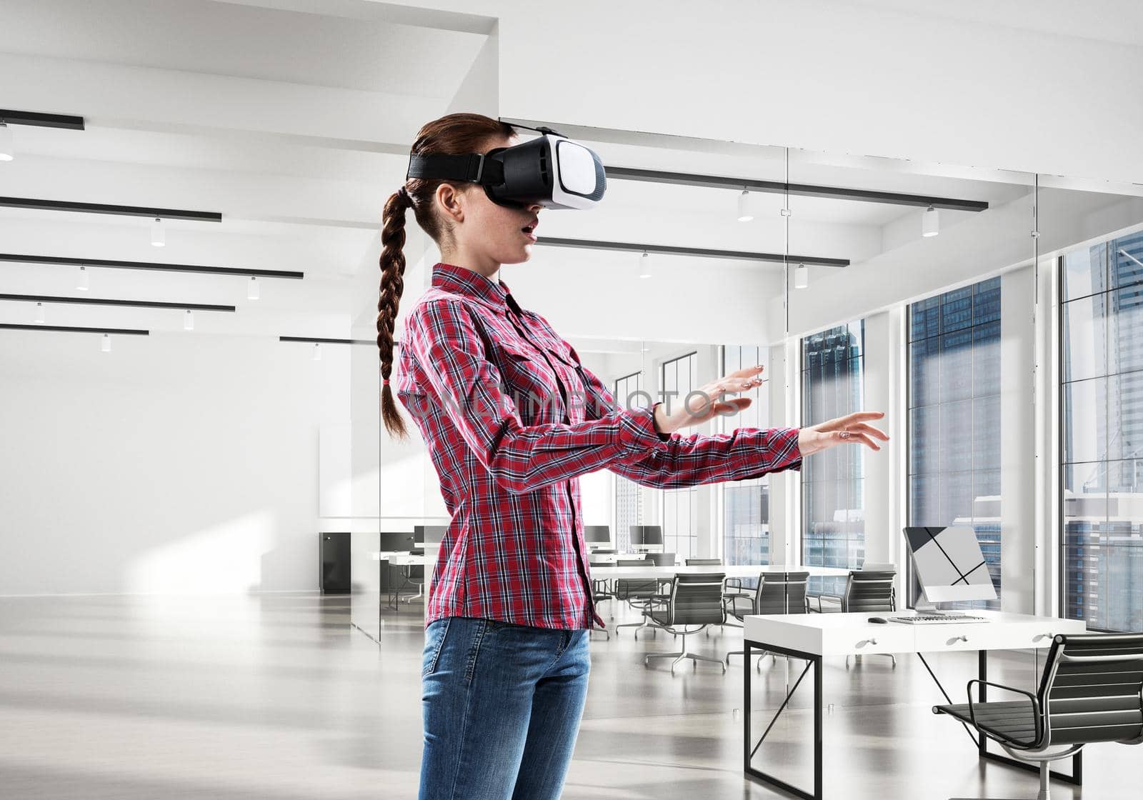 Young woman wearing virtual reality helmet in modern office interior. Mixed media