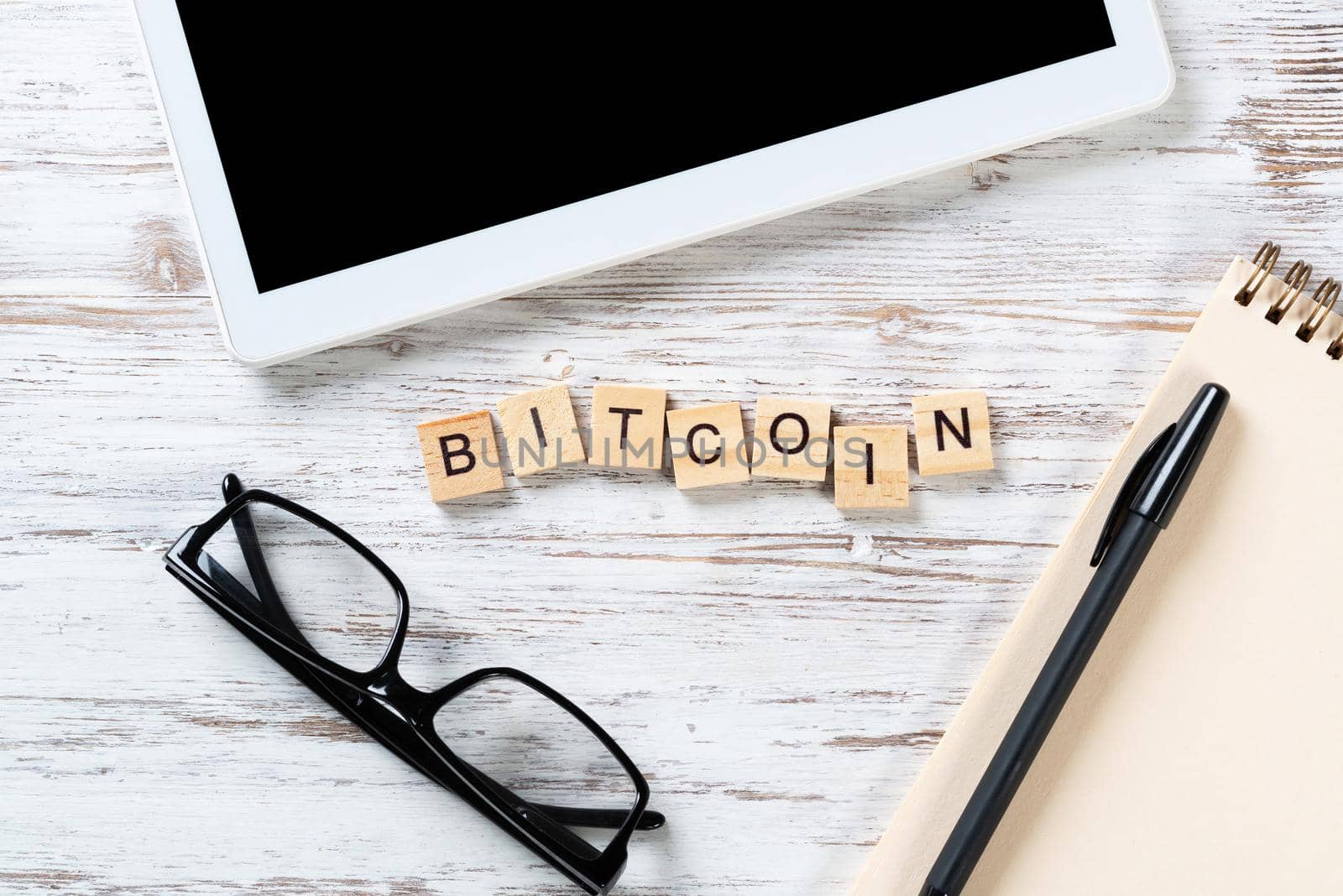 Bitcoin cryptocurrency concept with letters on cubes. Blockchain and digital money. Still life of workplace with supplies. Flat lay vintage wooden desk with tablet computer and spiral notebook.