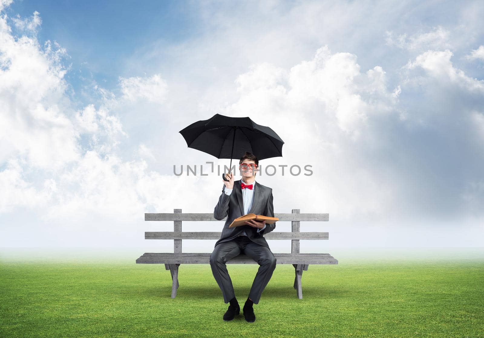 A young student holds a book and an umbrella. sits on a wooden bench