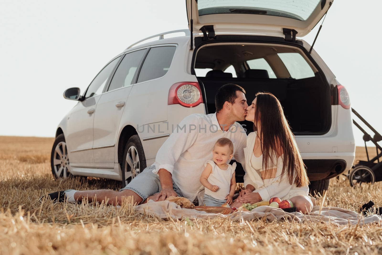 Young Family with Toddler Child Enjoying Picnic Outside City, Mom and Dad Kissing, They are Dressed Alike with Their Daughter, Weekend Road Trip with Car