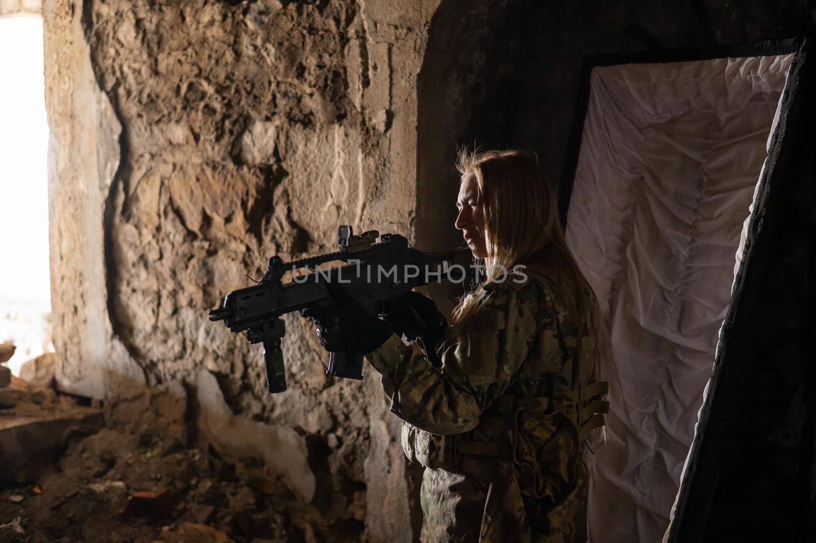 Caucasian woman in army uniform holding a machine gun and standing near an open coffin