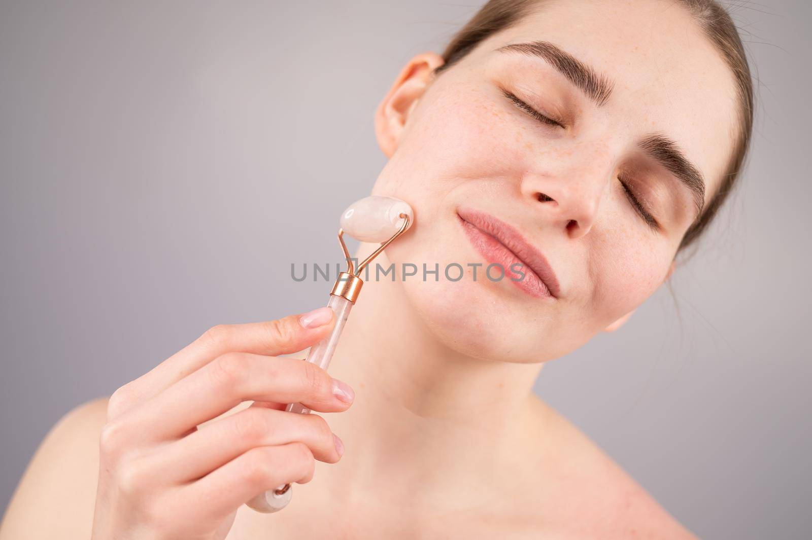 Close-up portrait of a woman using a quartz roller massager on her cheek for an alternative anti-aging