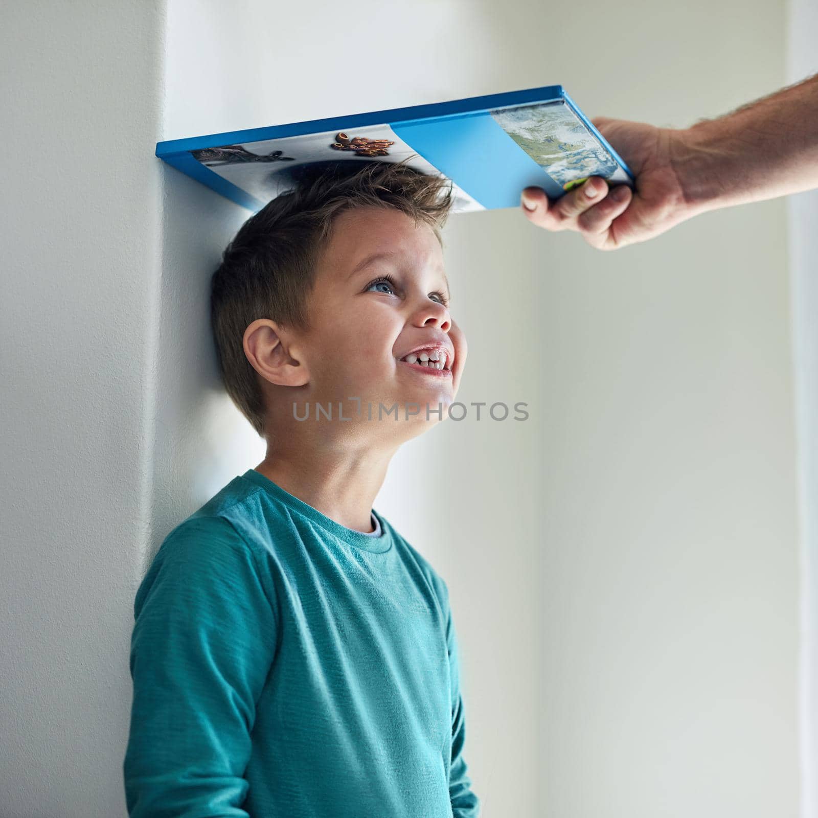 Cropped shot of a little boy getting his height measured against a wall with a book.